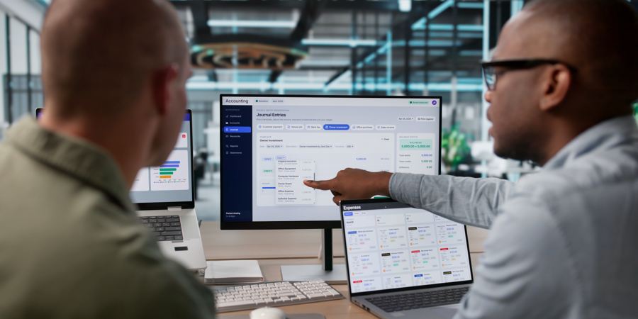 Two colleagues reviewing financial dashboards across multiple monitors
